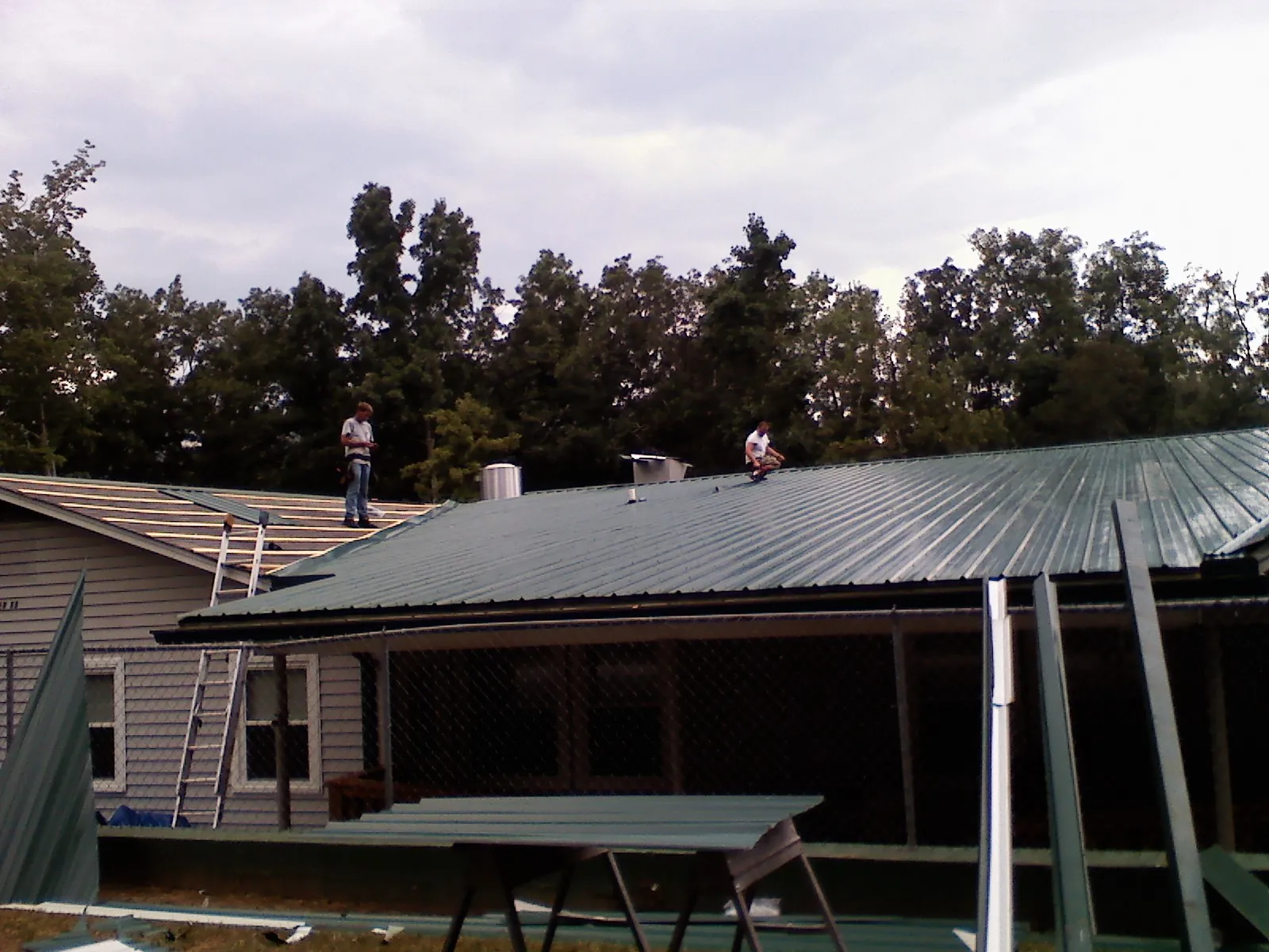 Two roofers installing green metal panels above a covered porch in Attica