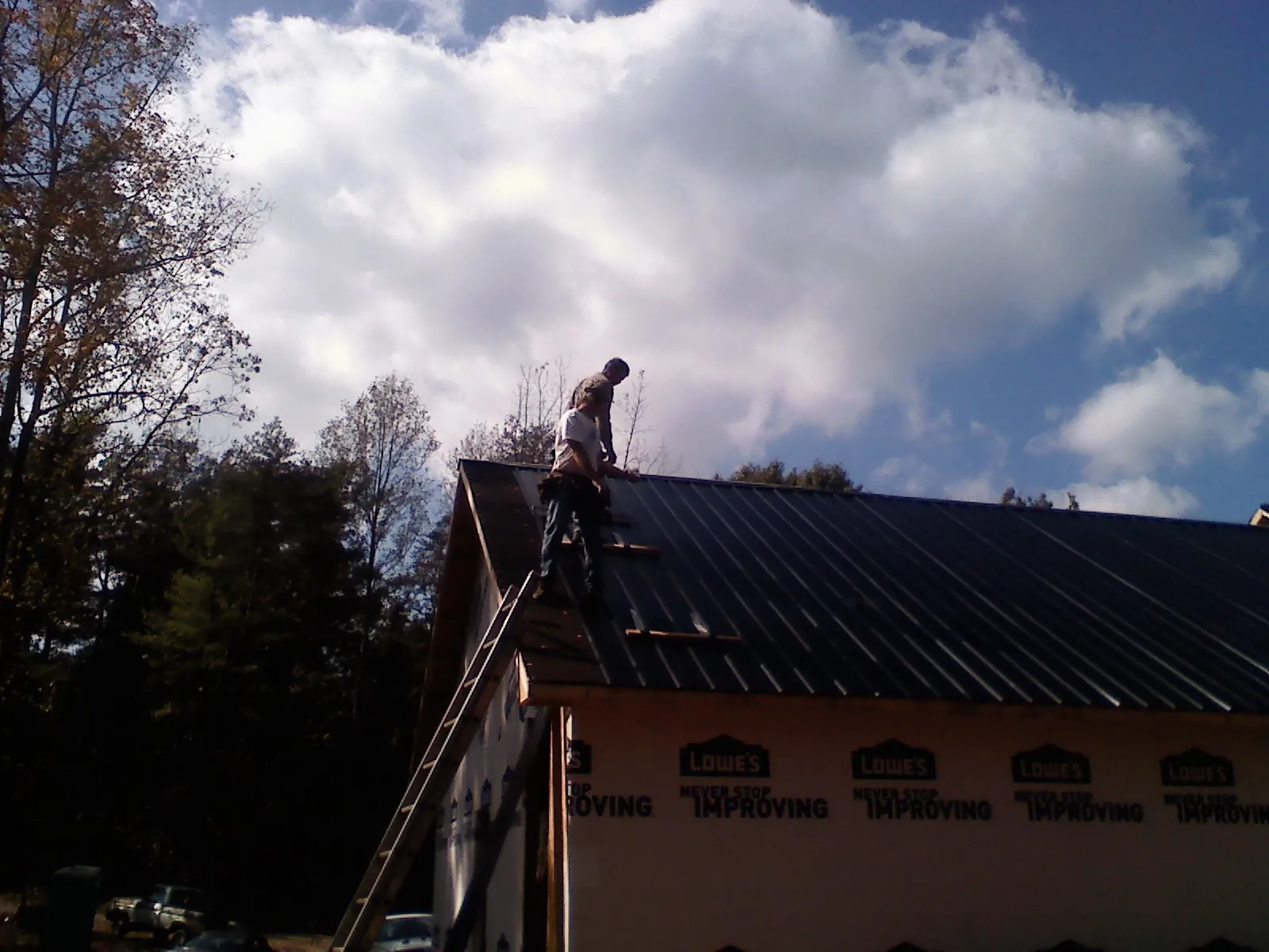 Roofer fastening dark metal panels high against a cloudy sky, from a Roof Inspection job in Attica
